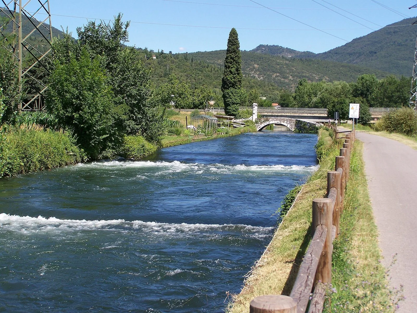 Il Naviglio Grande Bresciano a Gavardo: l'acqua limpida del canale corre fra le sponde verdi, con la pista ciclabile, un ponte ad arco in pietra e le colline boscose sullo sfondo